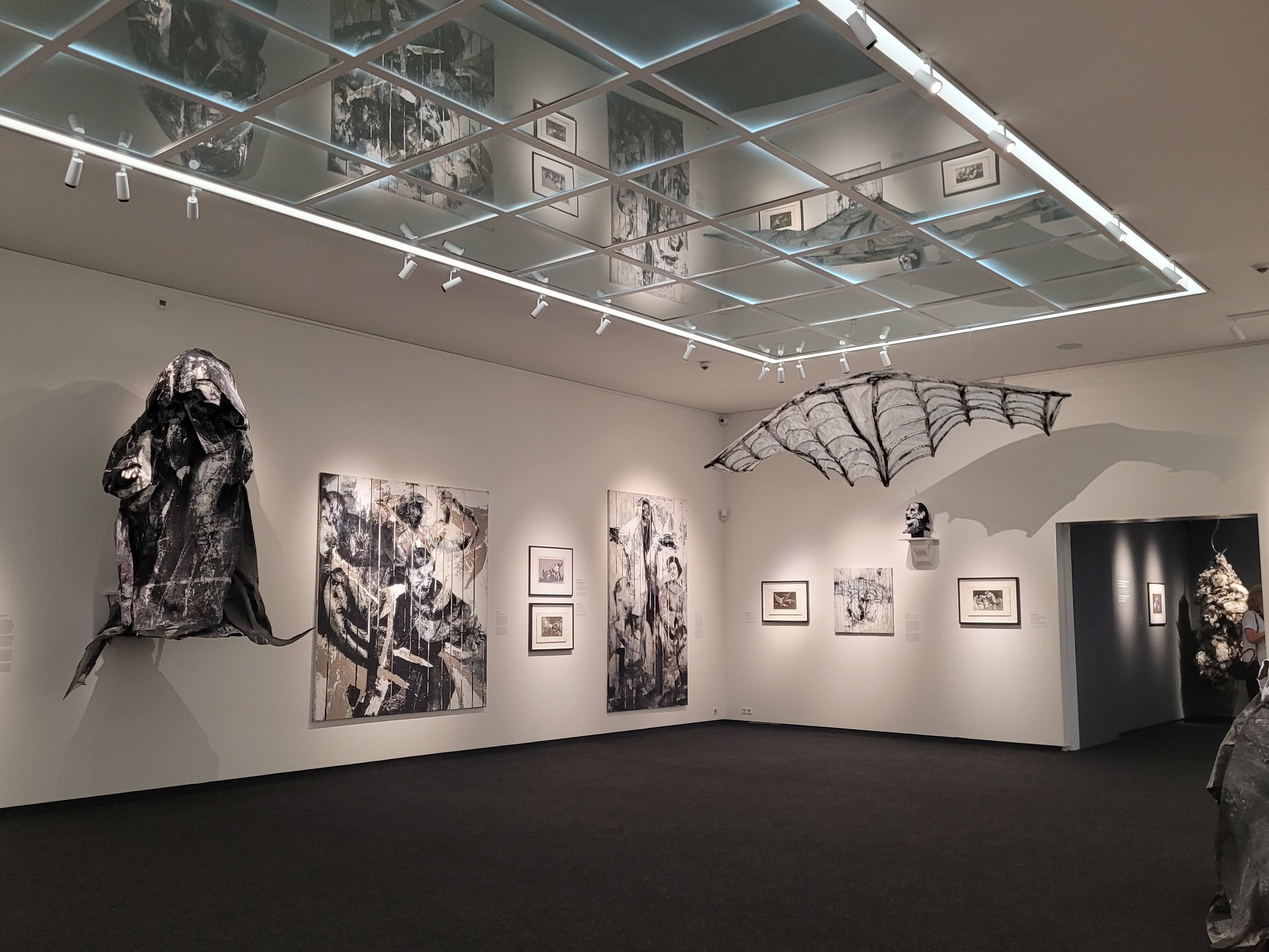 Salle d'exposition contenant des œuvres d'art en noir et blanc, avec des sculptures accrochées au mur et un plafond réfléchi.